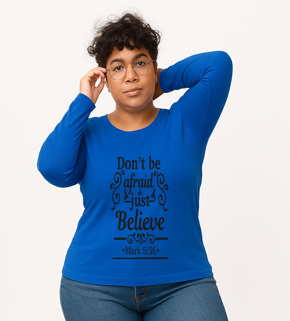 Cobalt Blue Christian long sleeve t-shirt with “Don’t Be Afraid Just Believe” Mark 5:36 scripture design, worn by woman in glasses and ripped jeans.