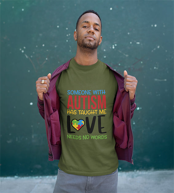 A man wearing a Olive T-shirt that says “Someone With Autism Has Taught Me Love Needs No Words,” featuring colorful text and a puzzle heart graphic.
