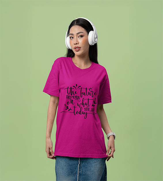 A woman wearing headphones and a magenta color T-shirt that reads “The Future Depends on What You Do Today” in a cursive black font, posing against a soft green background.