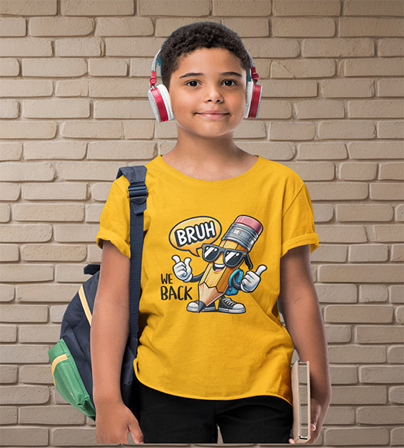 Young school-aged child wearing a gold t-shirt with a funny cartoon pencil graphic and the text “BRUH, WE BACK.” The kid is wearing headphones, holding a book, and standing in front of a beige brick wall. Ideal for back-to-school outfits