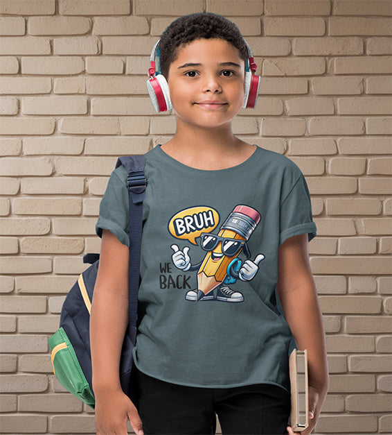 Young school-aged child wearing a dark grey t-shirt with a funny cartoon pencil graphic and the text “BRUH, WE BACK.” The kid is wearing headphones, holding a book, and standing in front of a beige brick wall. Ideal for back-to-school outfits
