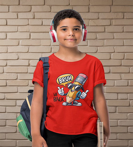 Young school-aged child wearing a red t-shirt with a funny cartoon pencil graphic and the text “BRUH, WE BACK.” The kid is wearing headphones, holding a book, and standing in front of a beige brick wall. Ideal for back-to-school outfits