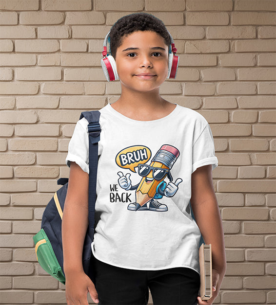Young school-aged child wearing a white t-shirt with a funny cartoon pencil graphic and the text “BRUH, WE BACK.” The kid is wearing headphones, holding a book, and standing in front of a beige brick wall. Ideal for back-to-school outfits