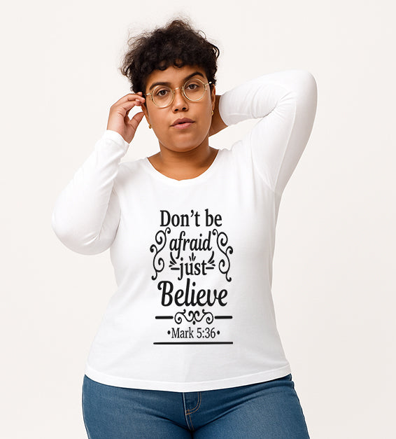 White Christian long sleeve t-shirt with “Don’t Be Afraid Just Believe” Mark 5:36 scripture design, worn by woman in glasses and ripped jeans.

