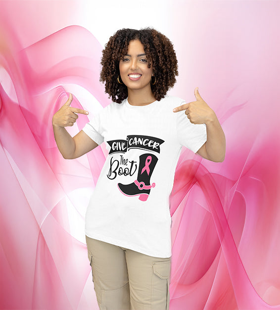 Woman wearing white “Give "C" the Boot” awareness T-shirt featuring a black cowgirl boot with a pink ribbon design, smiling and pointing at the design.