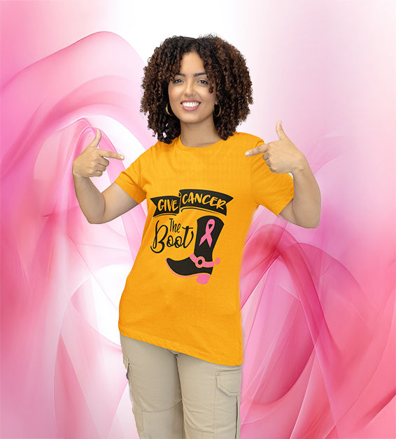 Woman wearing gold “Give C the Boot” awareness T-shirt featuring a black cowgirl boot with a pink ribbon design, smiling and pointing at the design.