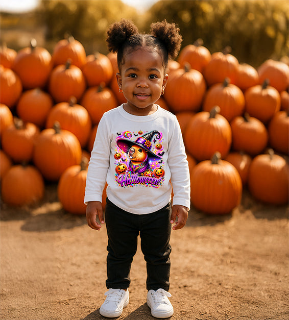 Toddler girl wearing white Halloween t-shirt with cartoon capybara witch design, pumpkins, sparkles, and the word Halloween in bold lettering