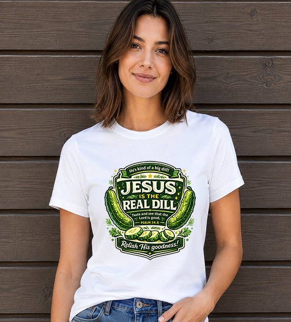 Woman wearing a white t-shirt featuring a humorous faith-inspired pickle illustration with Psalm 34:8 in front of a dark wooden wall.