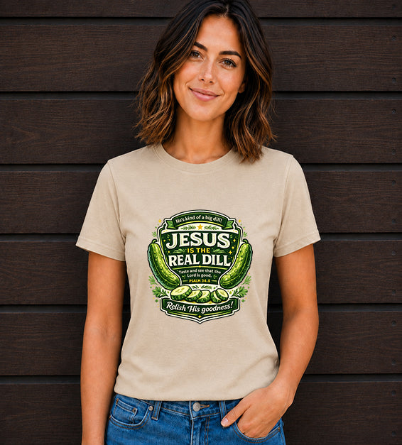Woman wearing a natural t-shirt featuring a humorous faith-inspired pickle illustration with Psalm 34:8 in front of a dark wooden wall.