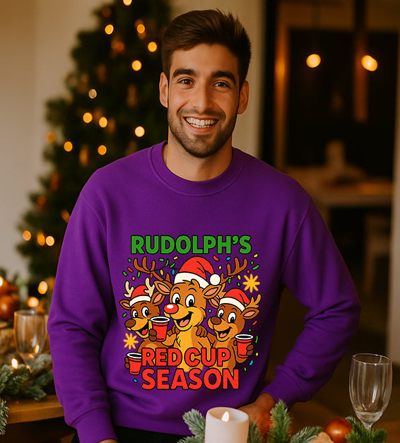 Man wearing a purple Christmas sweatshirt with a festive cartoon reindeer design and the text “Rudolph’s Red Cup Season” in bright holiday colors.