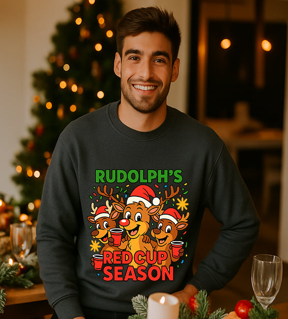 Man wearing a dark grey Christmas sweatshirt with a festive cartoon reindeer design and the text “Rudolph’s Red Cup Season” in bright holiday colors.