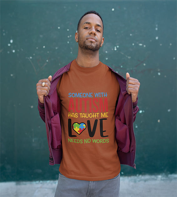 A man wearing a Chestnut T-shirt that says “Someone With Autism Has Taught Me Love Needs No Words,” featuring colorful text and a puzzle heart graphic.