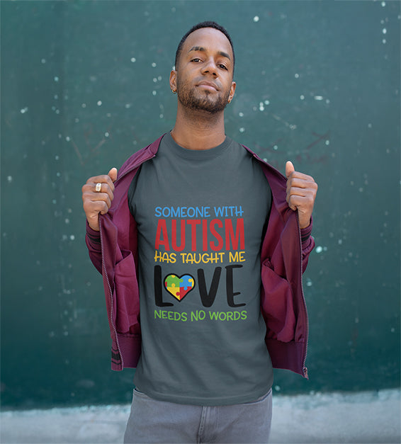 A man wearing a Dark Grey T-shirt that says “Someone With Autism Has Taught Me Love Needs No Words,” featuring colorful text and a puzzle heart graphic.