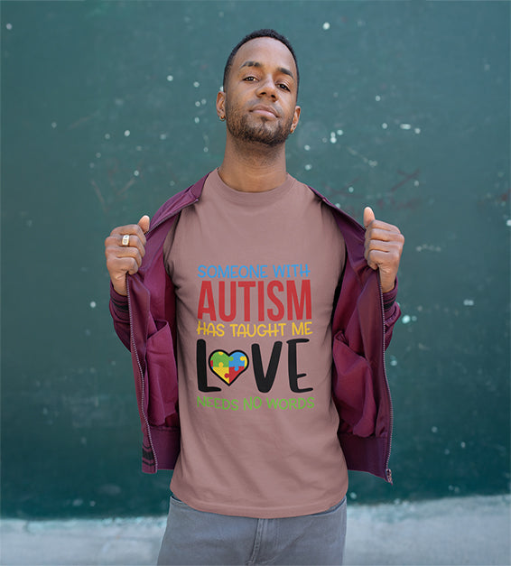 A man wearing a Mauve T-shirt that says “Someone With Autism Has Taught Me Love Needs No Words,” featuring colorful text and a puzzle heart graphic.