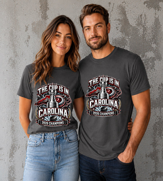 Asphalt t-shirt featuring The Cup Is In Carolina 2026 Champions hockey fan graphic with trophy, hockey puck, state outline, and championship artwork.