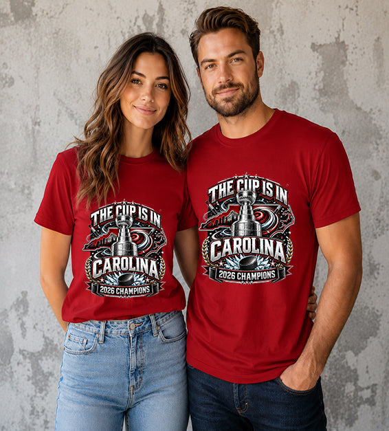 Canvas Red t-shirt featuring The Cup Is In Carolina 2026 Champions hockey fan graphic with trophy, hockey puck, state outline, and championship artwork.