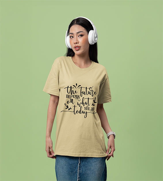 A woman wearing headphones and a soft cream color T-shirt that reads “The Future Depends on What You Do Today” in a cursive black font, posing against a soft green background.